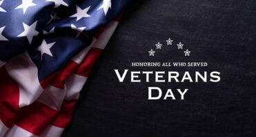 Happy Veterans Day. American flags with the text thank you veterans against a blackboard background.