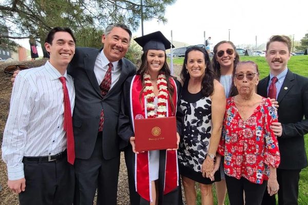 Santa Clarita Valley International (SCVi) School alum Emma Hild poses in graduation garb with her family outside while holding a red diploma from University of Utah.