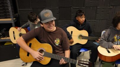 Santa Clarita Valley International students sit on chairs holding guitars.