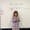 Santa Clarita Valley International (SCVi) School student stands in front of a classroom white board that says “My exit ticket heart word is” with a microphone in her hand.