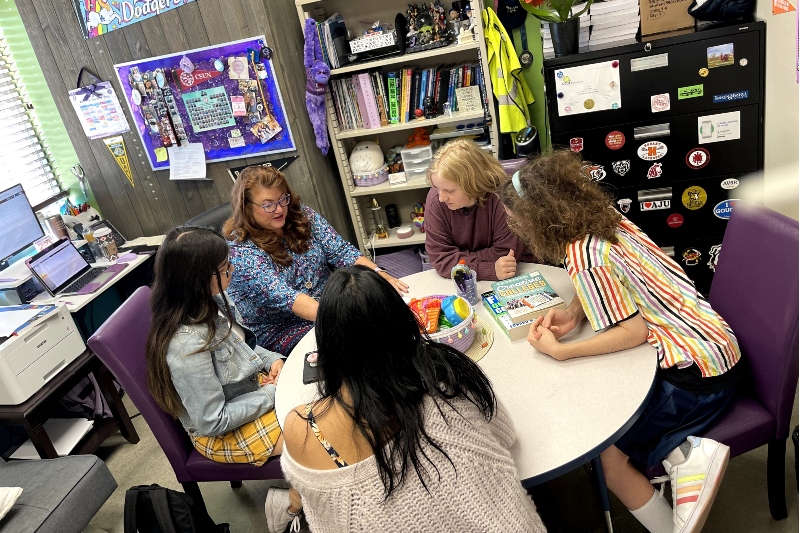 Santa Clarita Valley International (SCVi) Charter School teacher sits at a round table talking with four students.