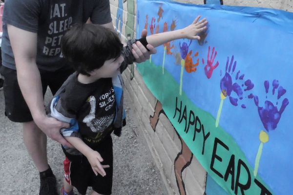 A small child takes their hand away from a Santa Clarita Valley International (SCVi) school blue banner where they pressed their handprint. A taller person is behind them guiding them.