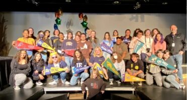 Santa Clarita Valley International (SCVi) Charter School seniors pose holding colorful flags of colleges they will attend after graduation.