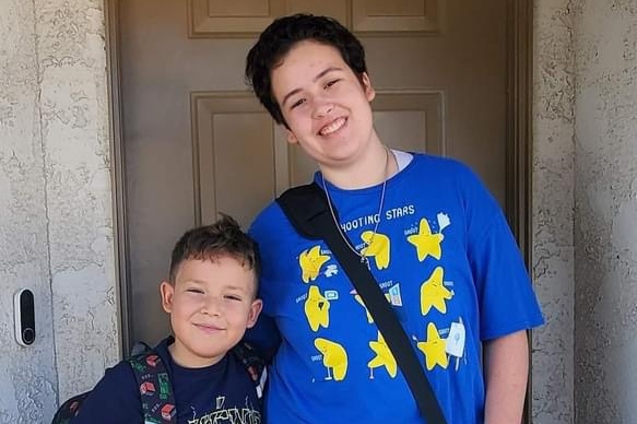 Santa Clarita Valley International (SCVi) Charter School students stand in front of a doorway wearing bags slung over their shoulders and hugging side by side while smiling.